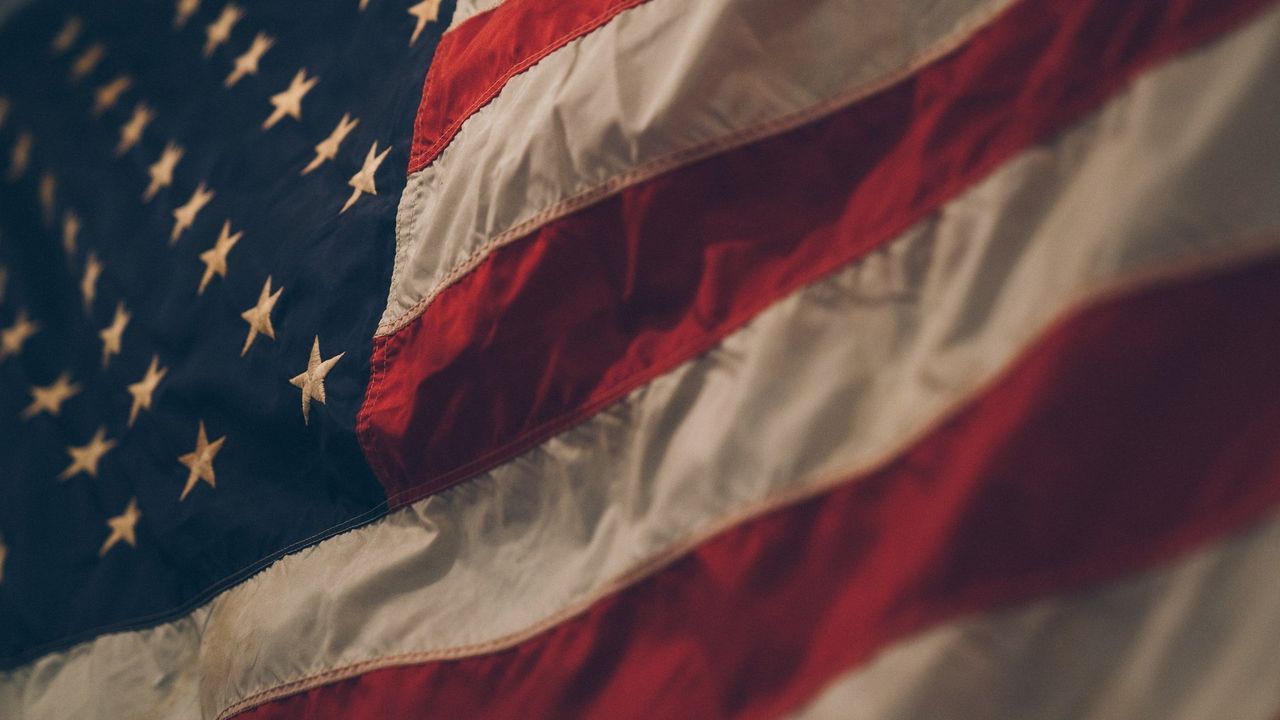 Closeup image of an American flag showing red and white stripes, and white stars on a blue background. The image has a dark and moody feel.