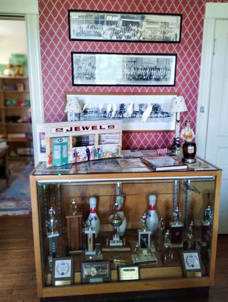 A photograph of a trophy case in the main room of the Kincaid House featuring Jewel merchandise and trophies.