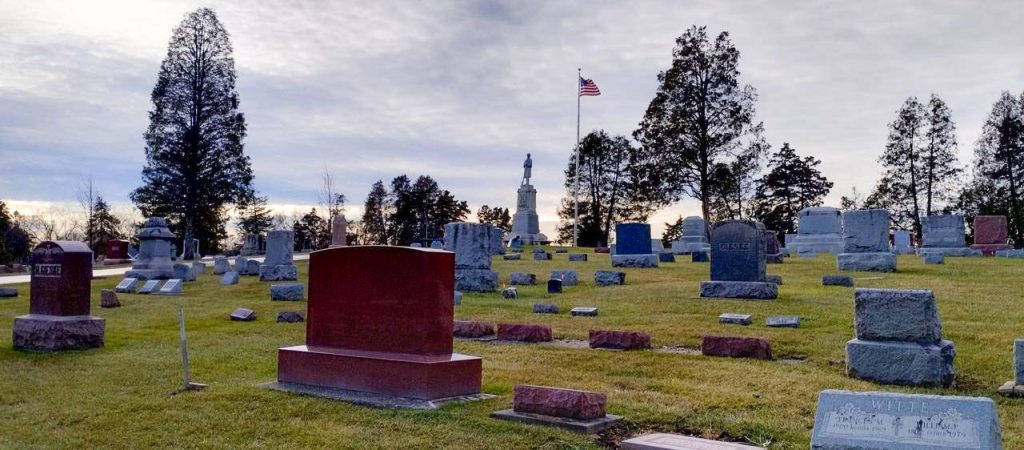 A photograph of gravestones in Evergreen Cemetery. An American flag is flying in the background.