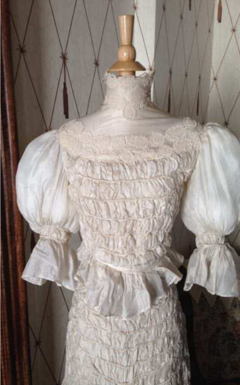 Picture of an antique white wedding dress on a dress stand.